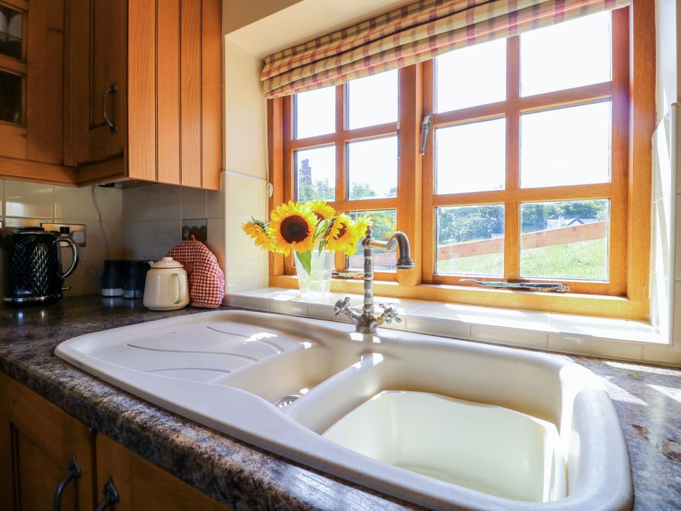A kitchen sink with sunflowers and a window at Bluebell Barn in Oakamoor