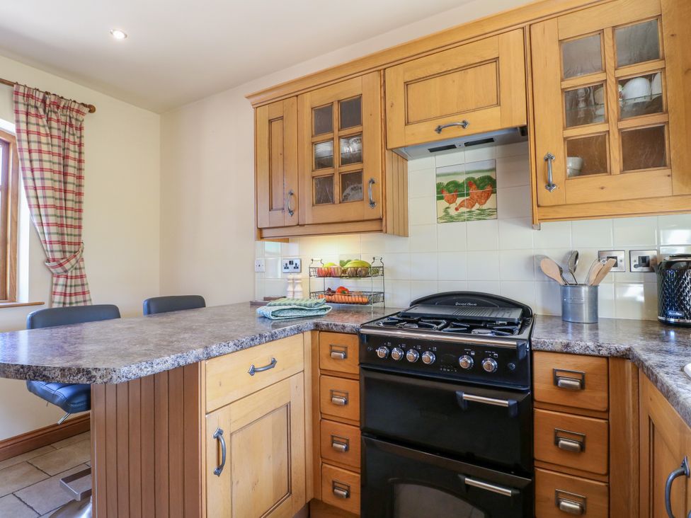 A kitchen with a stove, cabinets and bar stools at Bluebell Barn in Oakamoor