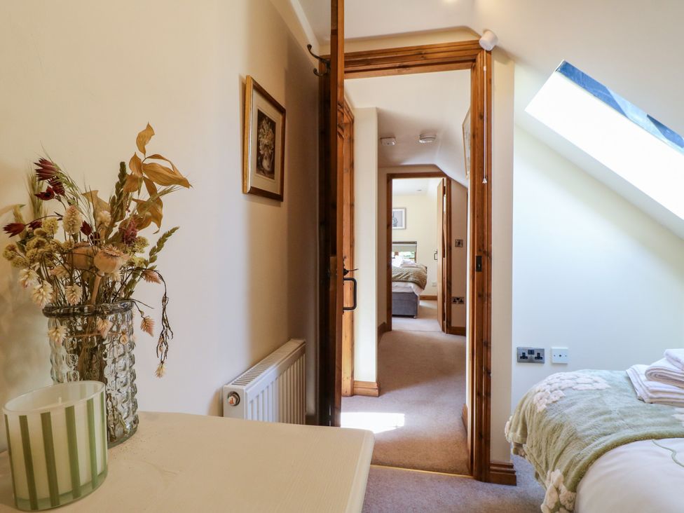 A bedroom with a vase of dried flowers and a view into another room at Bluebell Barn in Oakamoor