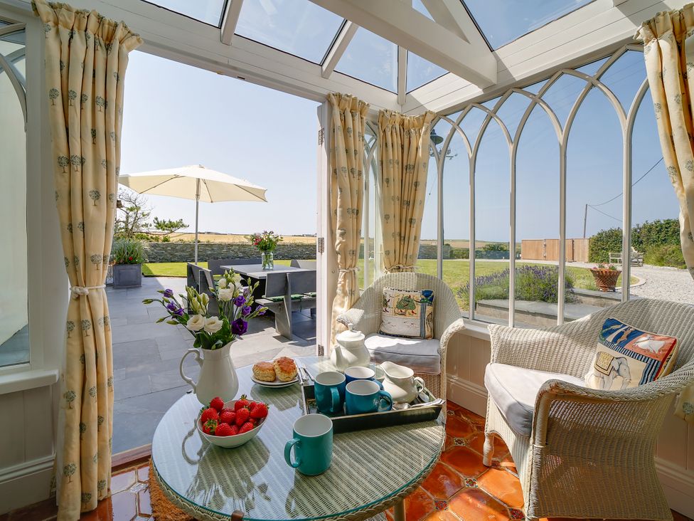 A conservatory with a table and chairs overlooking a garden at Porthcothan House St Merryn