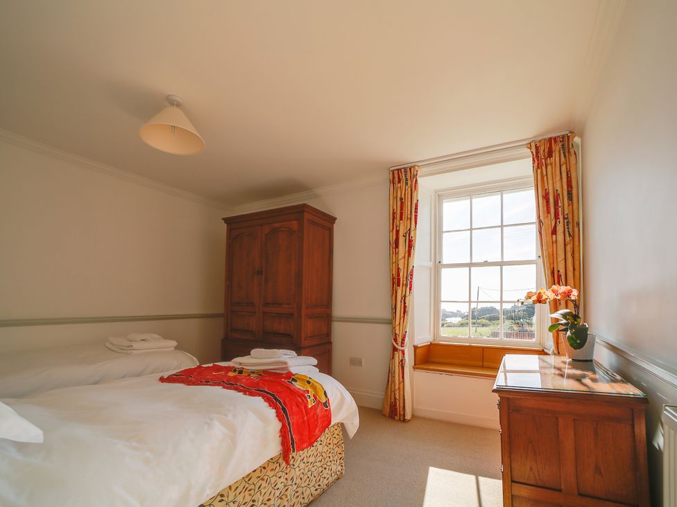 A bedroom with two beds and a wardrobe at Porthcothan House in Porthcothan