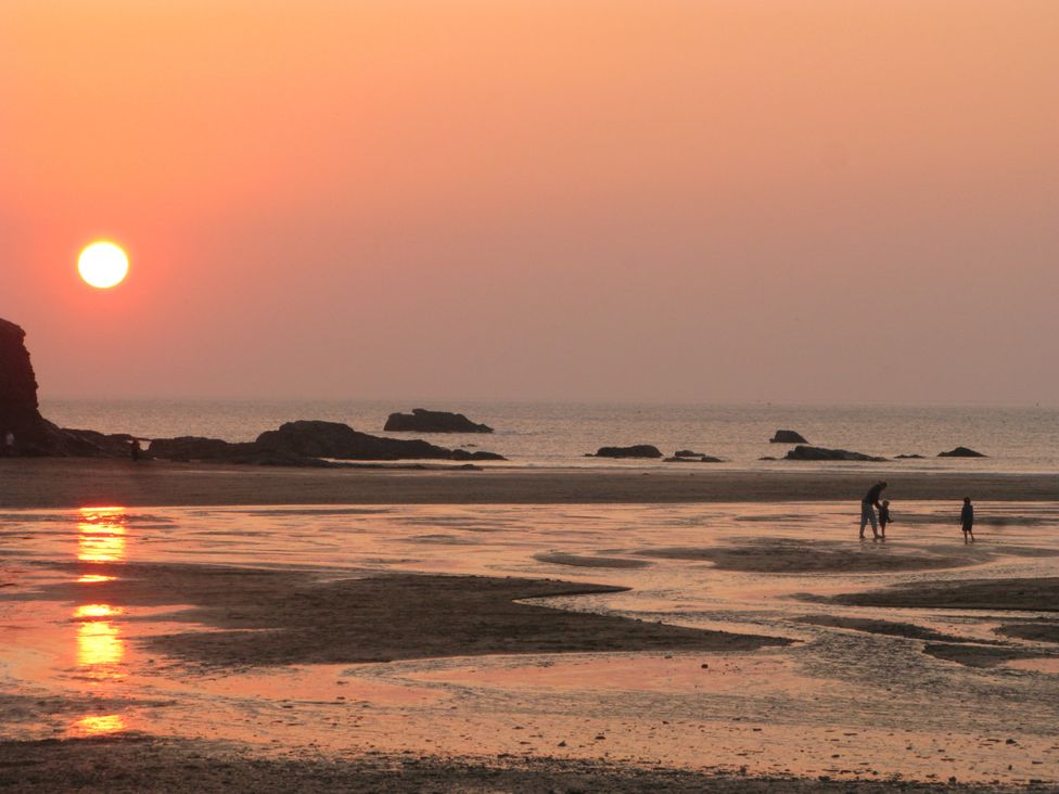 A beach scene with a sunset and people on the sand at Porthcothan House in Porthcothan