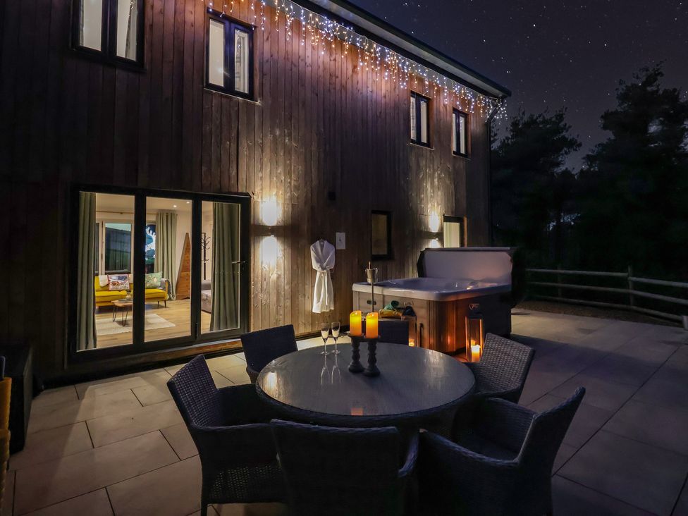 An outdoor area with a dining table and hot tub at Stag Cottage in Lytchett Matravers