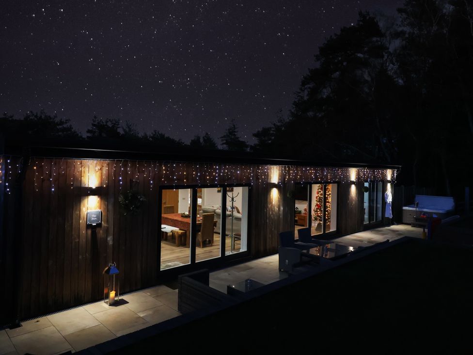 An exterior view of a house at night with lights and a Christmas tree at The Barn in Lytchett Matravers