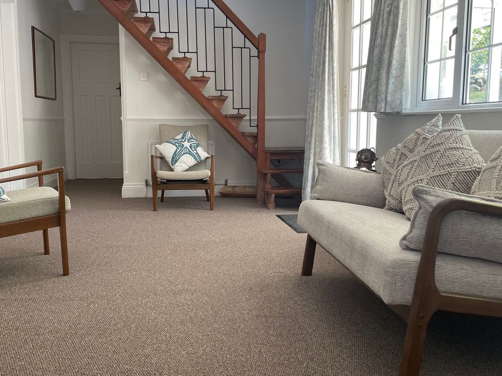 A living room with wooden chairs, a sofa with cushions, carpeted floor, wooden stairs, and windows with curtains at Rocklea Seaside Cottage in Newcastle County Down