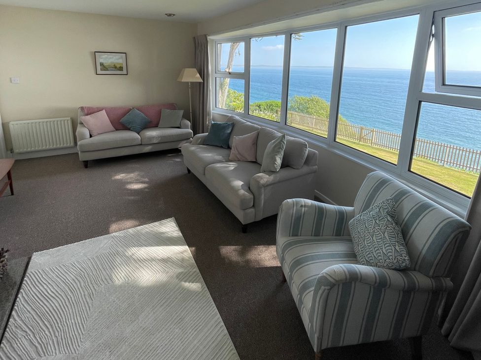 A living room with sofas and armchair facing large windows with a sea view at Rocklea Seaside Cottage in Newcastle County Down