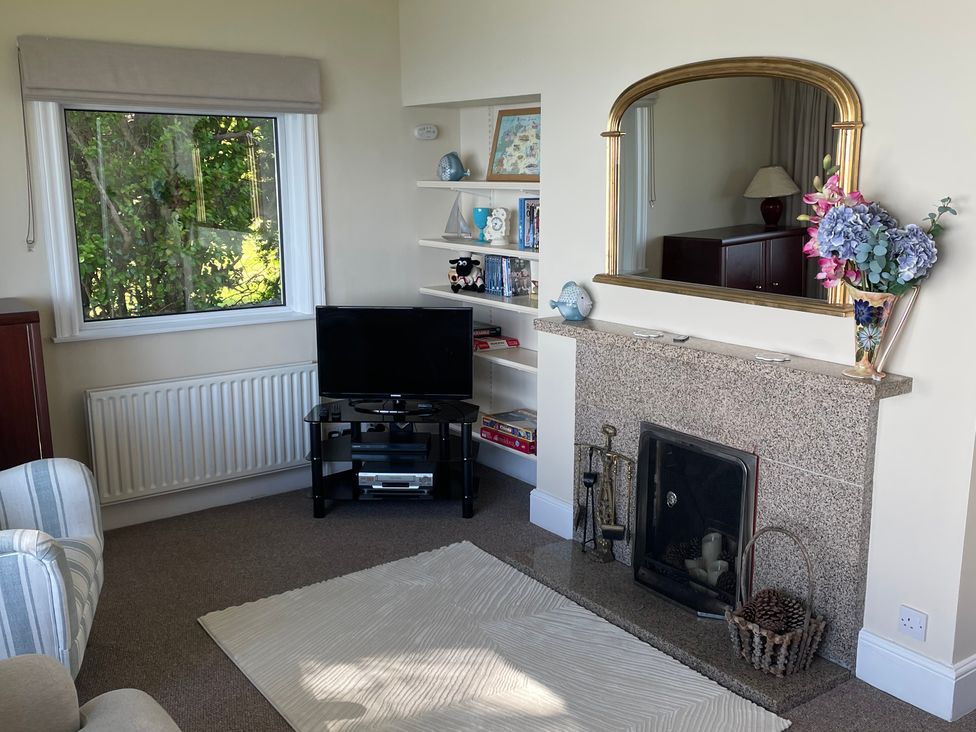 A living room with a fireplace mirror TV shelf and armchair at Rocklea Seaside Cottage in Newcastle County Down