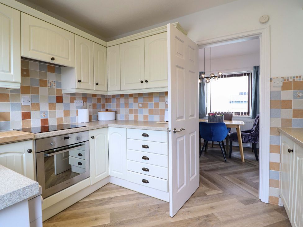 A kitchen with white cabinets and a doorway to a dining area at Ser a Mor (Stars and Sea) Bull Bay near Amlwch