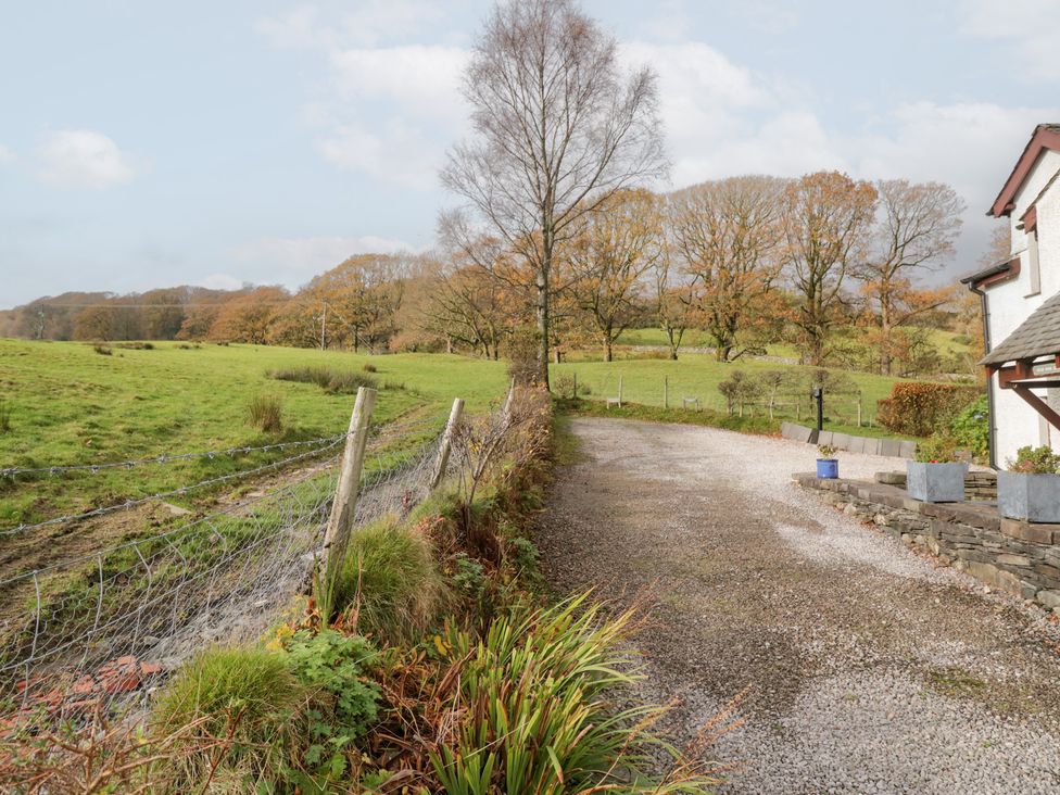 A gravel driveway next to a barbed wire fence with grass and trees at Low Dow Crag in Coniston