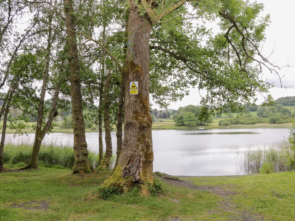 A view of a lake with trees and a warning sign at Low Dow Crag in Coniston