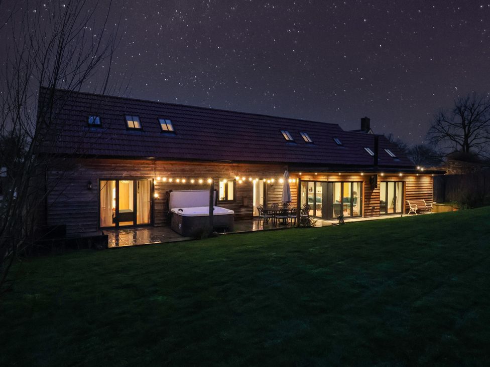 An outdoor view of a house with a hot tub and deck lights at The Gully in Sherborne