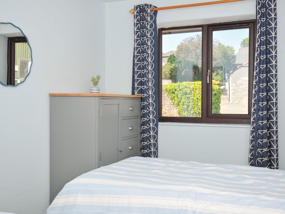 A bedroom with a bed, window, cabinet, and mirror at Columbine Cottage in Bude