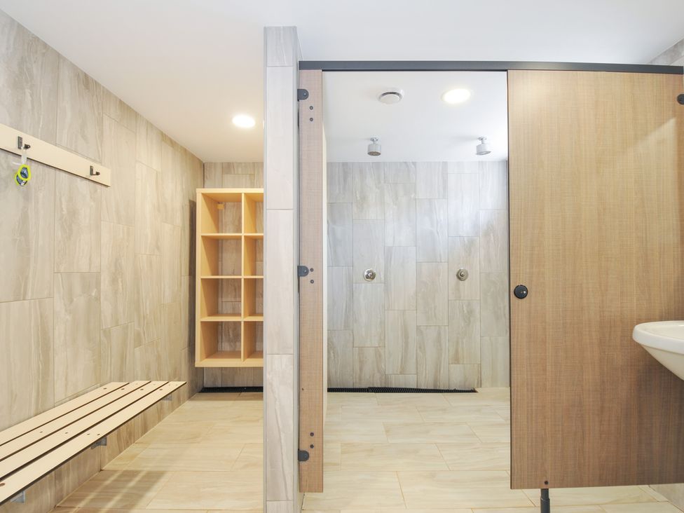 A bathroom with a shower area and storage shelves at Columbine Cottage in Bude