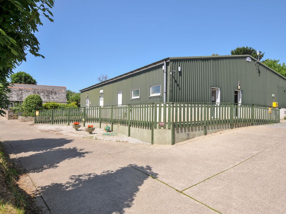 A green building with a fence and parking area at Columbine Cottage in Bude