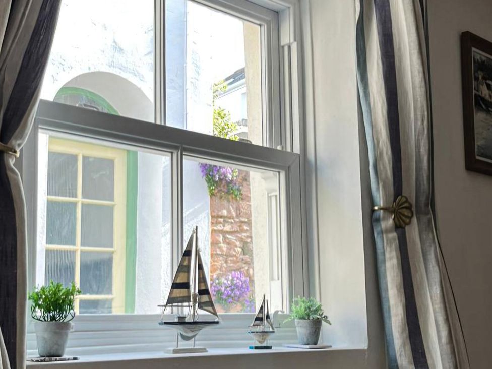 A window with sailboat decor and potted plants at Honeymoon Cottage in Appledore