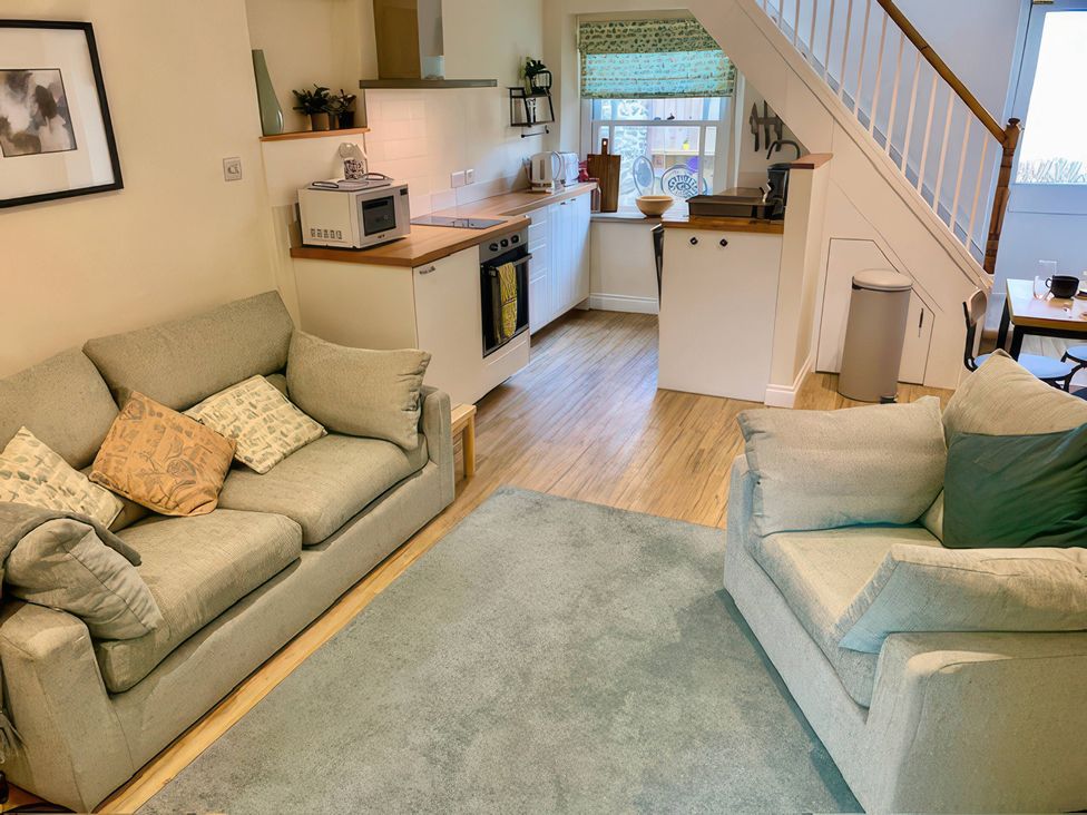 A living room with sofa and kitchen area at Bobbin Cottage in Swanage