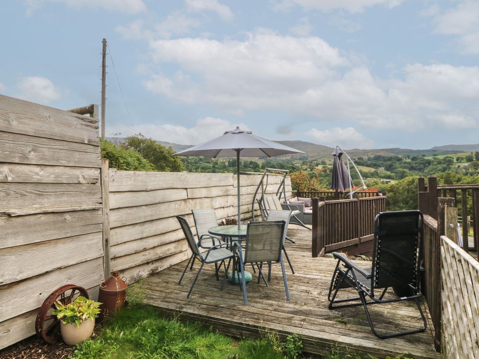 A deck with a table and chairs under an umbrella at Beudy Penarddwnion in Rhydymain near Dolgellau