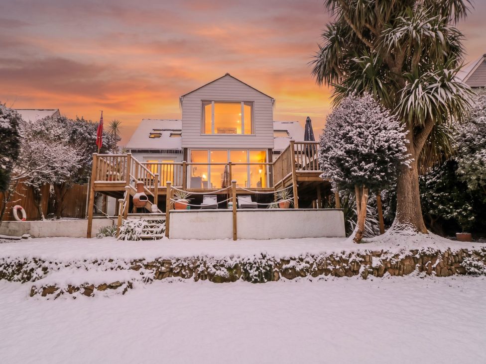 A house with a deck and trees in a snow-covered garden at Trewartha Beach House in Praa Sands