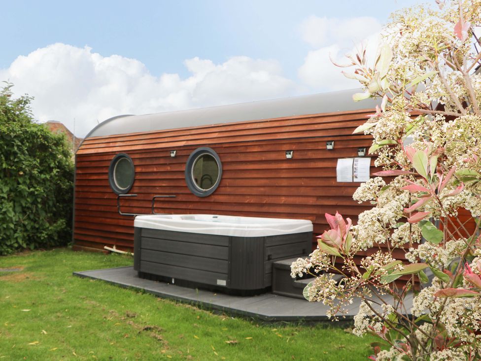 A garden with a hot tub next to a wooden building with round windows at Willow Pod in Arundel West Sussex
