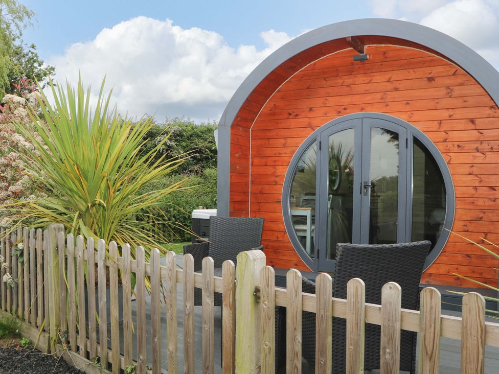 A wooden pod with round doors and outdoor seating behind a wooden fence at Willow Pod in Arundel West Sussex