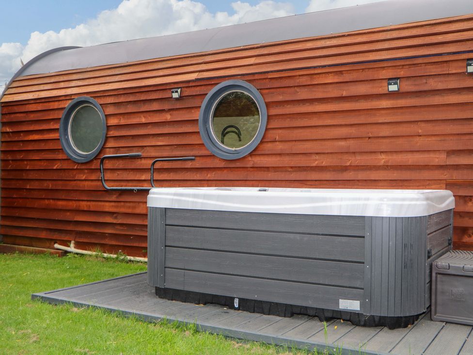 An outdoor hot tub next to a wooden building with two round windows at Willow Pod in Arundel West Sussex