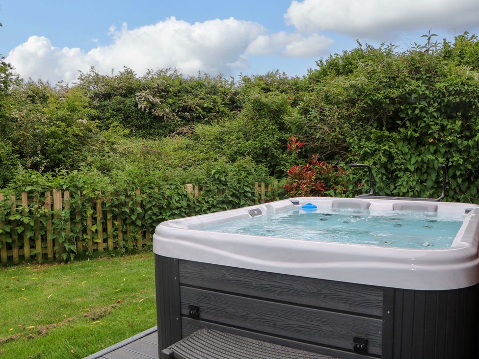 An outdoor hot tub on a deck next to a green garden with a wooden fence at Willow Pod in Arundel West Sussex