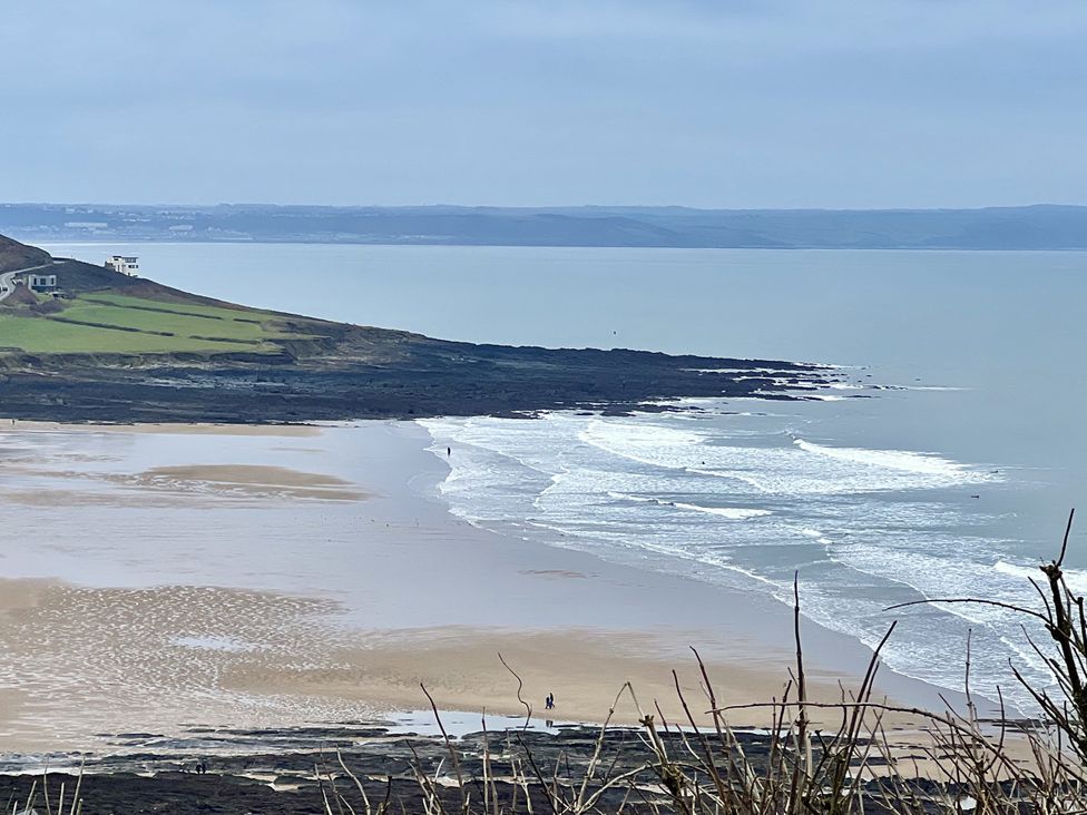 A beach scene with waves and a house on a hill at Beechcroft Cottage in North Molton