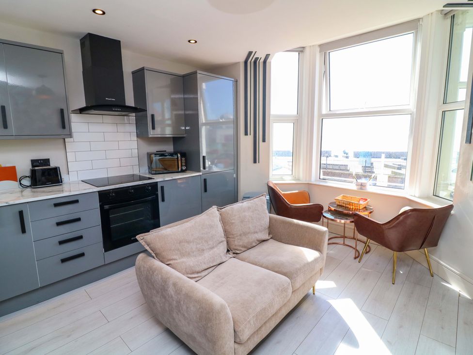 A kitchen with cabinets, stove, sofa, and chairs at Apt 4 @ Hunter's Quay, Bridlington