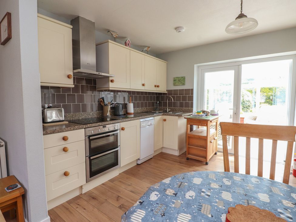 A kitchen with cabinets, appliances and a dining table at Bro Mebyd in Criccieth