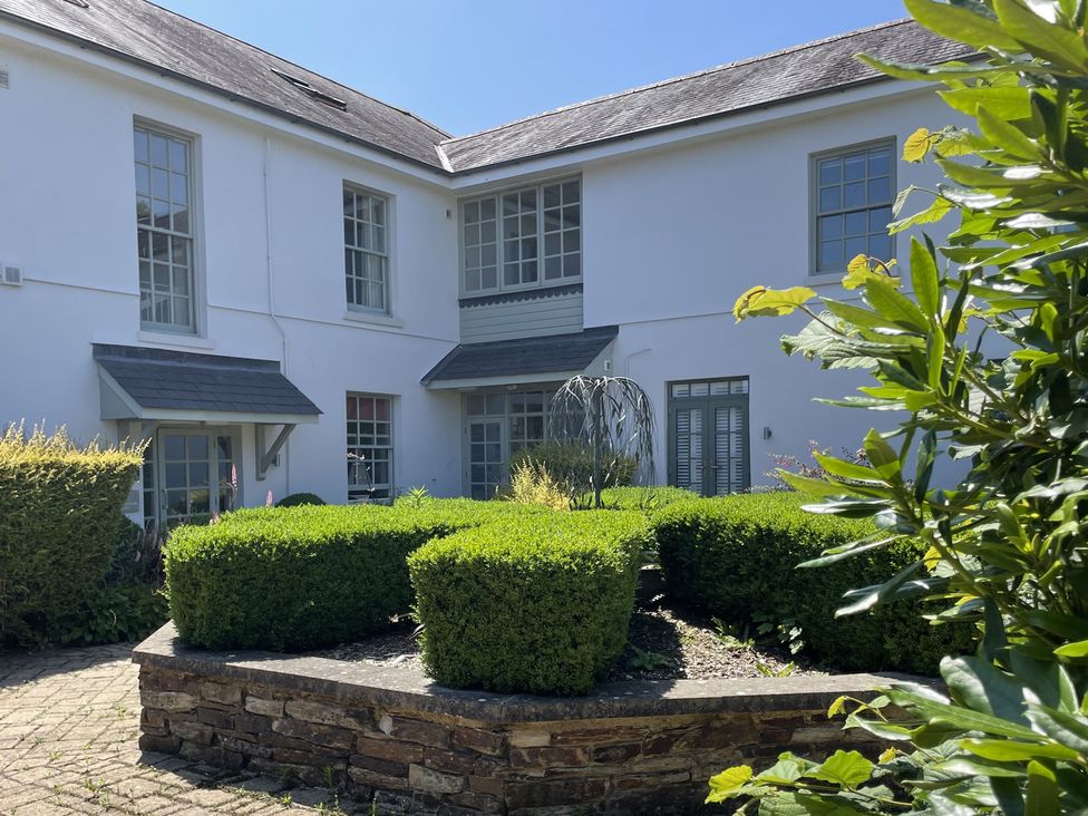A garden with well-trimmed bushes and a building in the background at 2 The Manor House, Hillfield Village Dartmouth