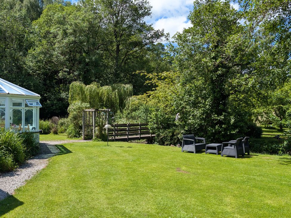 A garden with chairs and a conservatory at Little Pandy Cottage Afonwen near Caerwys