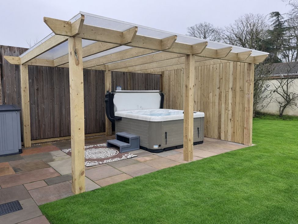 A garden with a hot tub under a wooden pergola at Daisy Tree Cottage in Woodhall Spa