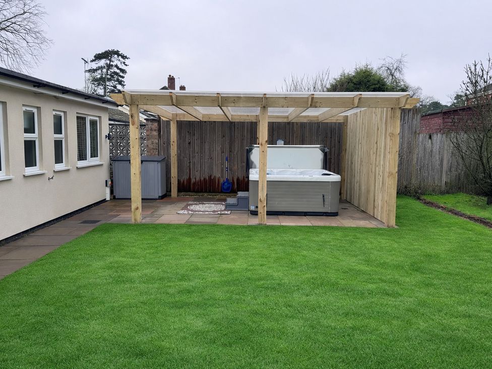 A garden with a hot tub under a pergola at Daisy Tree Cottage in Woodhall Spa