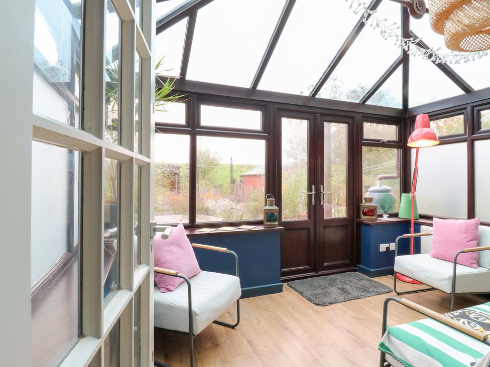 A conservatory with seating and plants at Coastguard Cottage in Rye