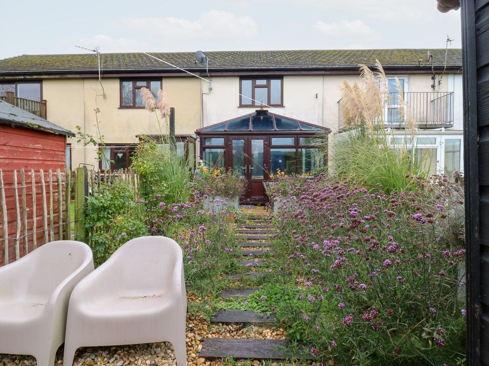 A garden with flowers and a path leading to a conservatory at Coastguard Cottage in Rye