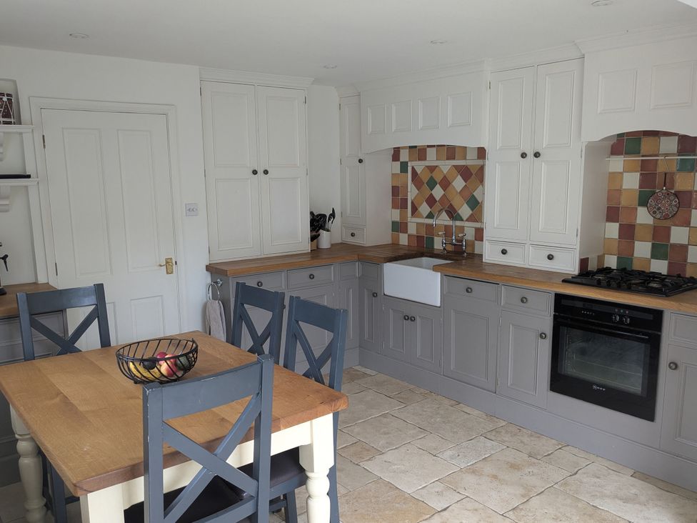 A kitchen with cabinets and a dining table at Mill Stream Cottage in Lower Slaughter near Bourton-On-The-Water