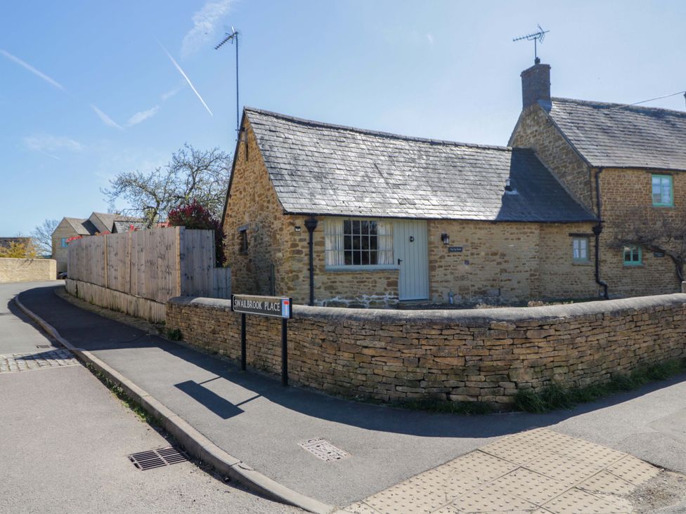 A cottage with a stone wall and a street sign at Swalbrook Place in Kingham