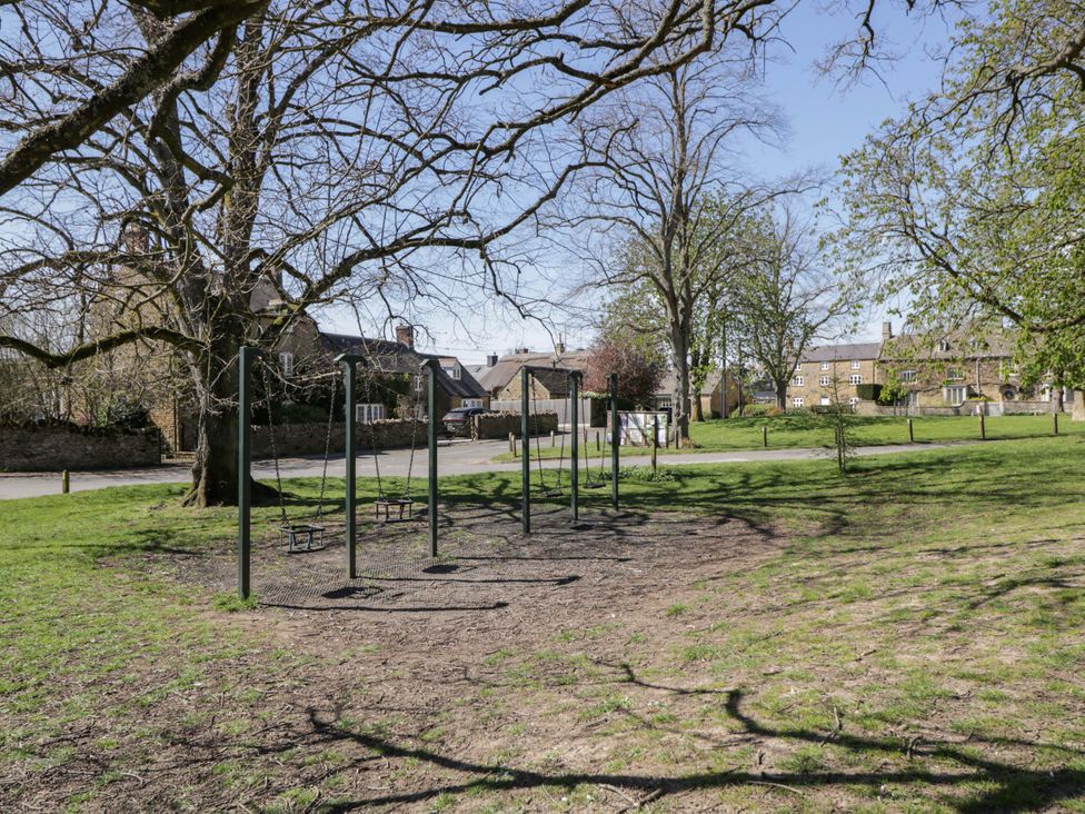 A park with a swing set and trees at The Tap Room in Kingham