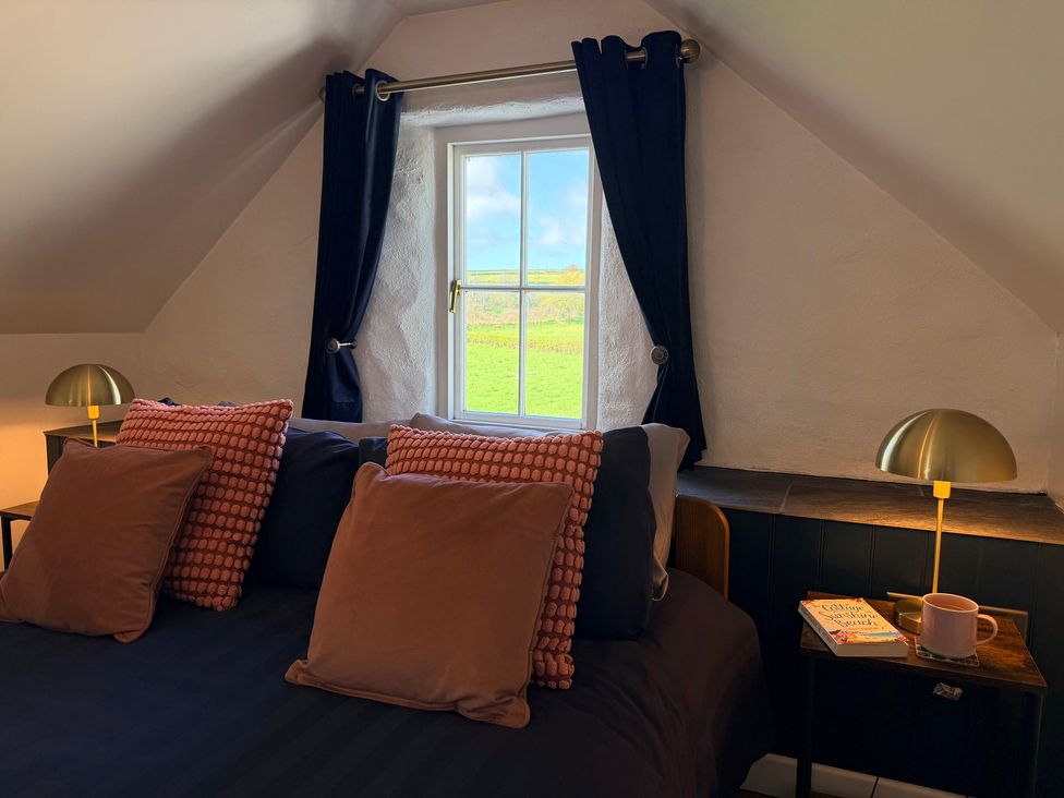 A bedroom with a bed, cushions, and a window at Pensarngerrig in Rhydlewis