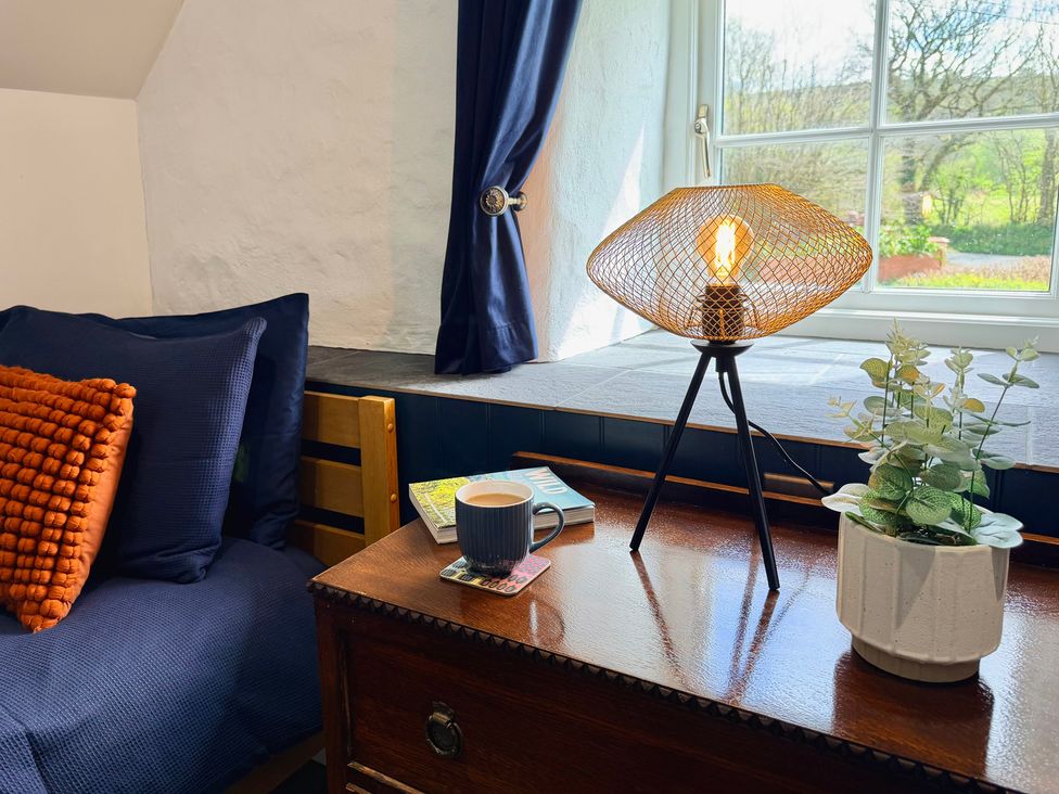 A bedroom with a bed, lamp, coffee cup, and plant at Pensarngerrig in Rhydlewis