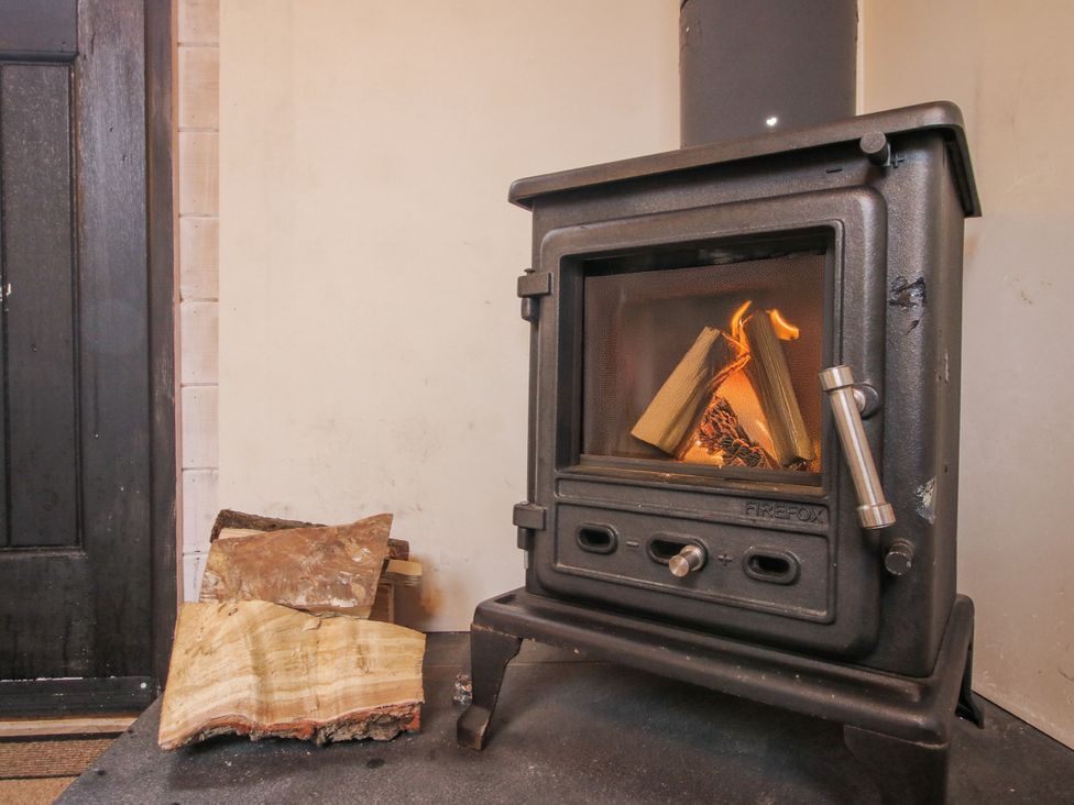 A wood stove with firewood in a living room at Aston - Shepherd Hut Aston On Clun