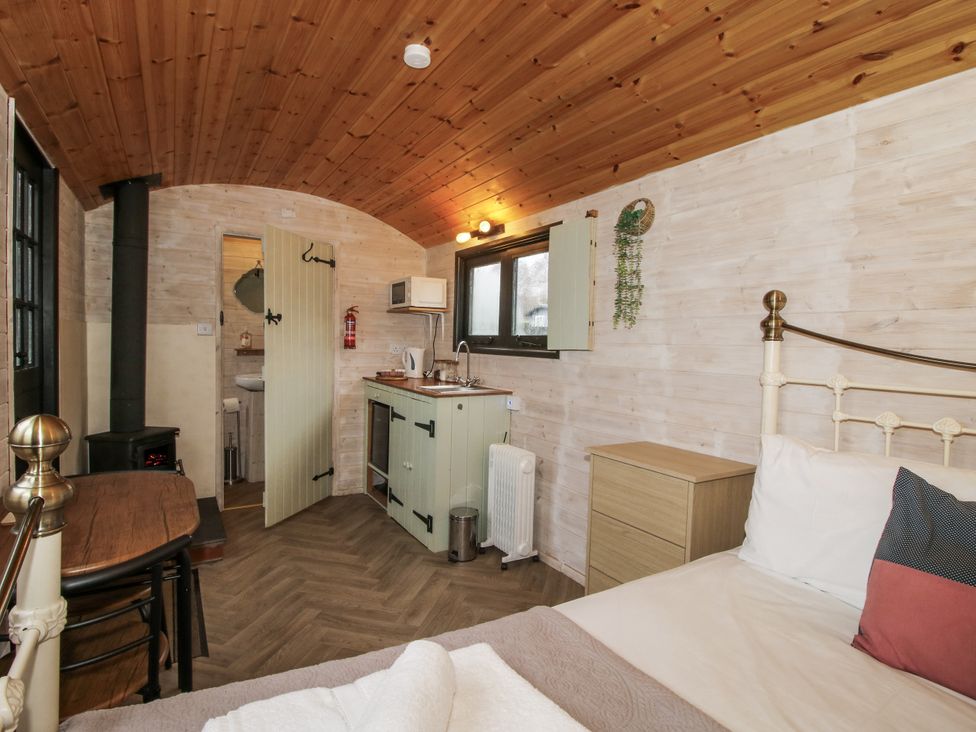 A bedroom with a bed, table, and kitchen unit at Aston - Shepherd Hut Aston On Clun