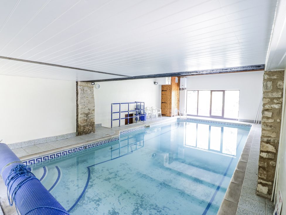 An indoor pool with chairs and a shelving unit at Dairy Cottage in Witney