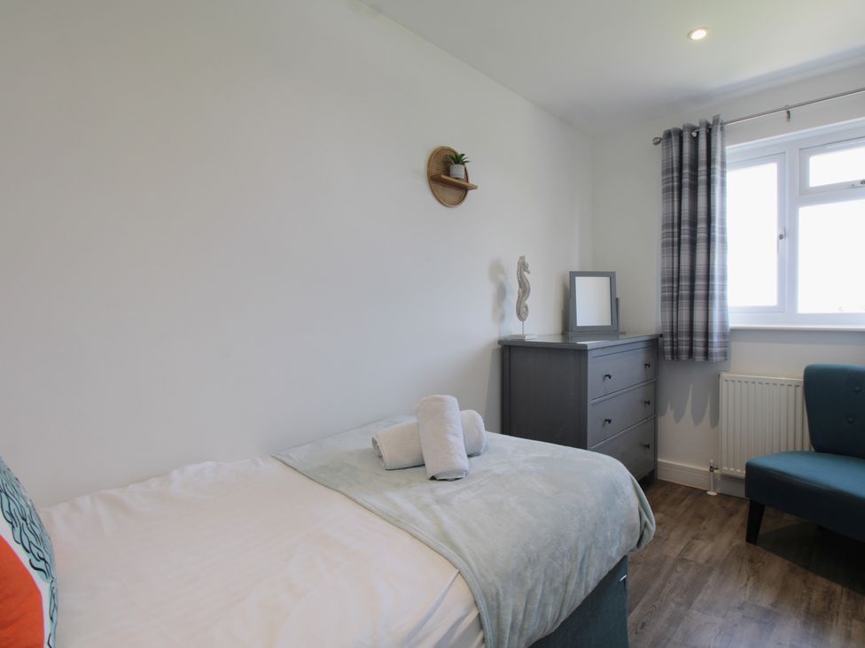 A bedroom with a bed, dresser, chair, and towels at 65 Channel View in Ilfracombe