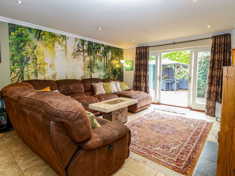 A living room with a sofa, coffee table, and large windows at Birch Cottage in Brundall