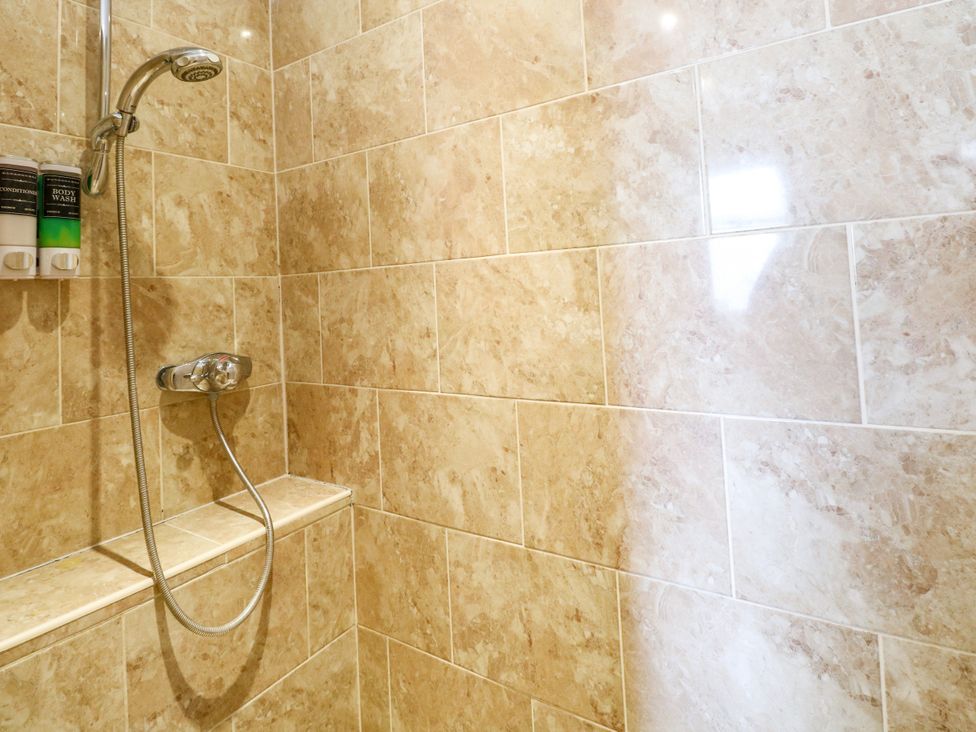 A shower with tiles and soap dispensers at Birch Cottage in Brundall