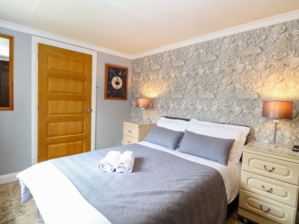 A bedroom with a bed and nightstand at Birch Cottage in Brundall