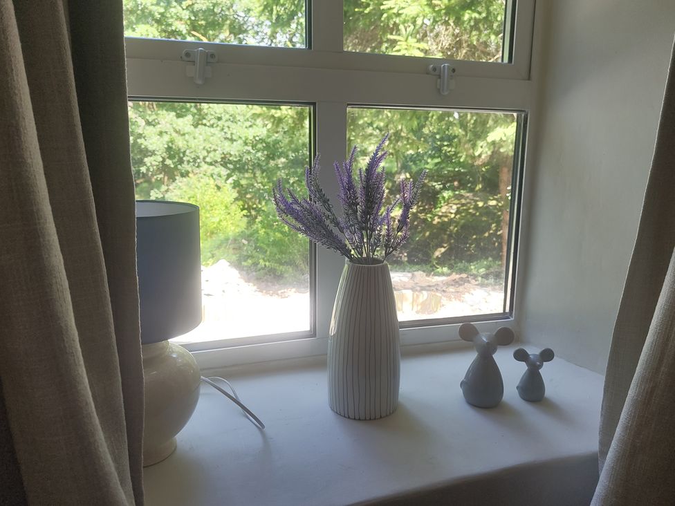 A windowsill with a lamp, vase, flowers, and figurines at Islwyn near Bala