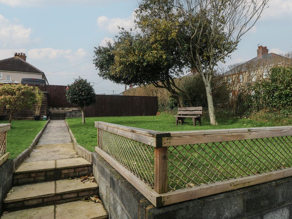 A garden with grass, trees, a bench, and a pathway at Brynawel in Burry Port