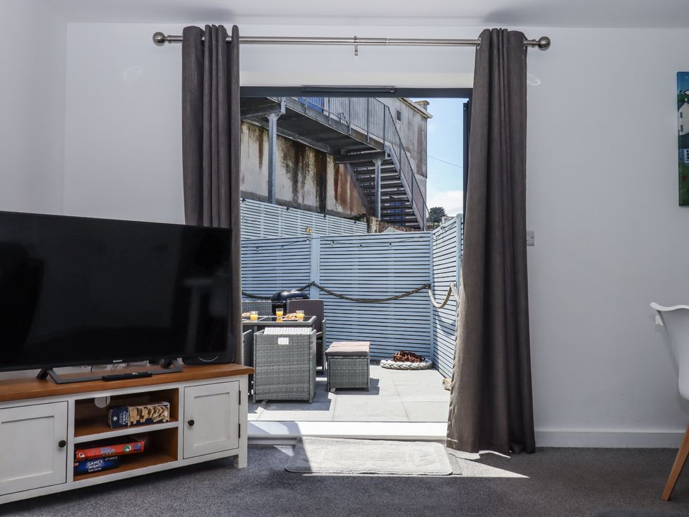 A living room with a television and a view of a patio at Driftwood in Torquay